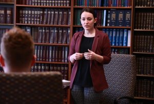 a student speaks to a professor in front of a wall of books