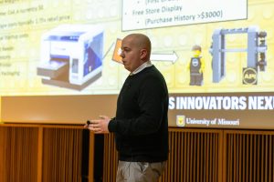 a photo of parker owens giving his business pitch during the competition with a slide of his business details behind him