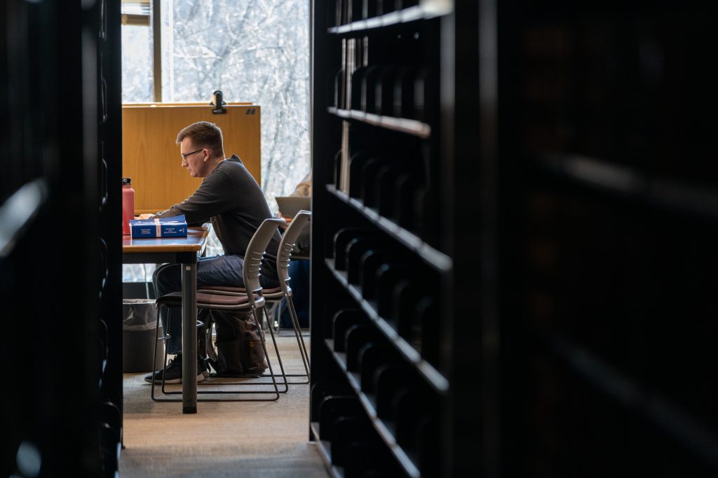a photo of a male student studying in the library between bookcases