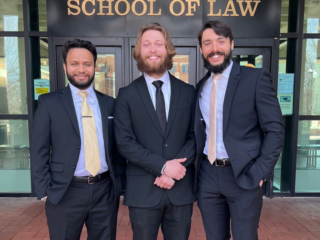 a photo of three mizzou law students standing in front of the door to hulston hall