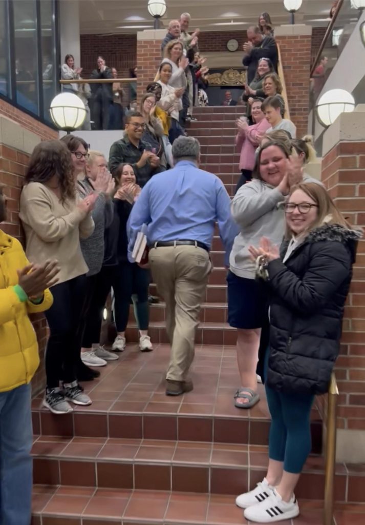 a photo of a professor walking up stairs through a tunnel of people clapping