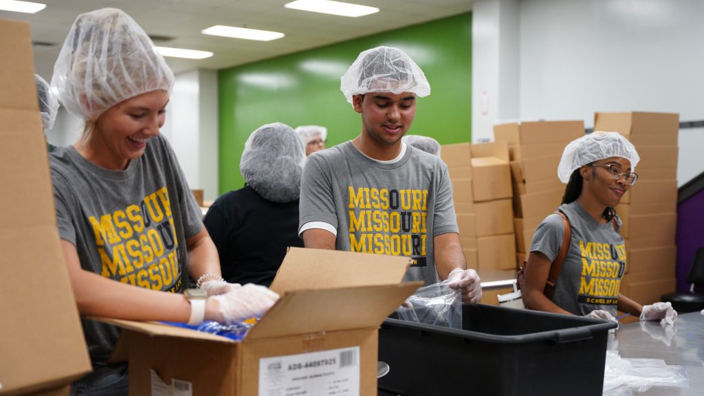 a photo of students working at a food bank wearing hair nets