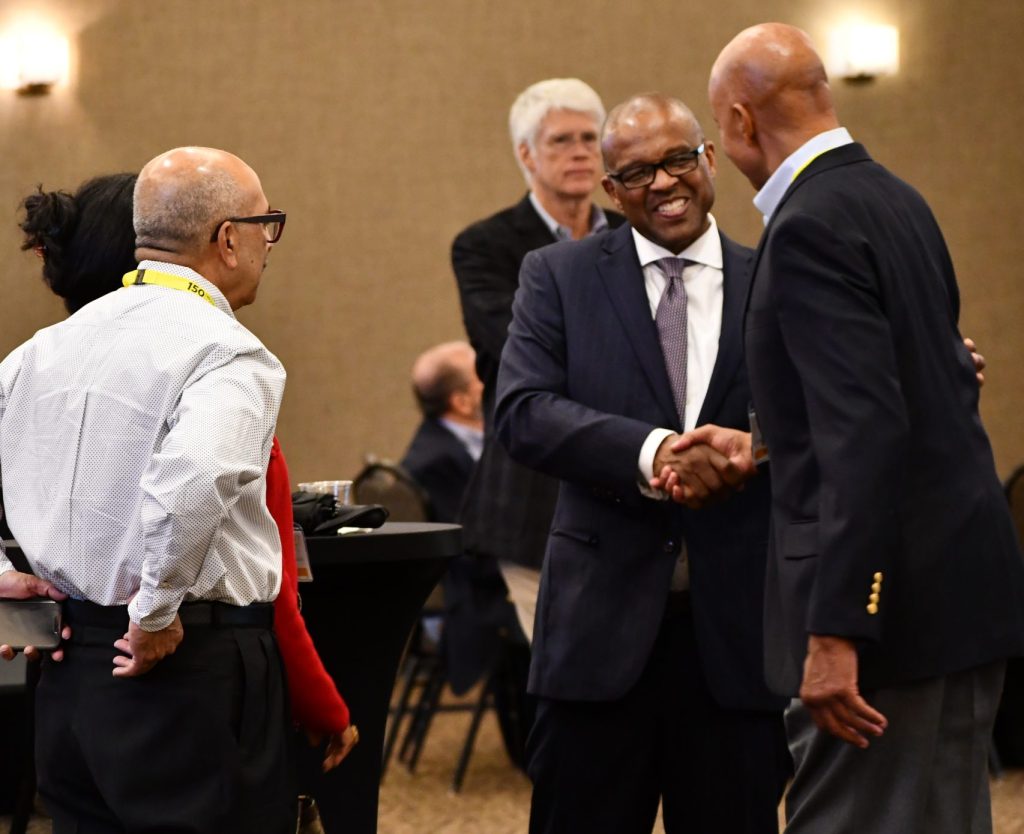 a photo of three alumni speaking and shaking hands